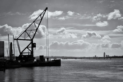 Silhouette crane by sea against sky