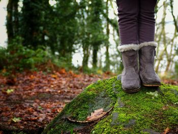 Low section of woman wearing fur boots while standing on rock in forest
