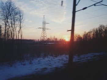 Silhouette trees and electricity pylon against sky during sunset