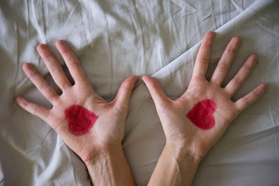 Cropped hands of woman with heart shape drawing on bed