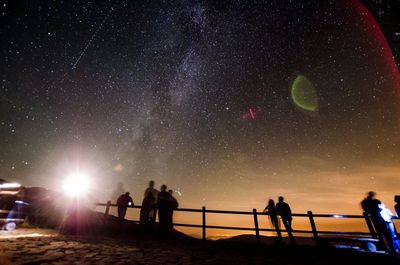 Low angle view of people at observation point against star field