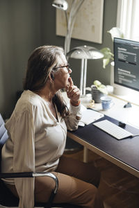 Side view of mature female freelancer with disability sitting at desk in home office