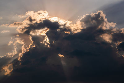 Low angle view of sunlight streaming through clouds