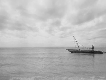 Fisherman standing in boat over sea against sky