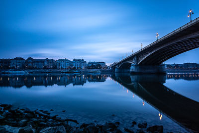 Bridge over river in city against blue sky at dusk