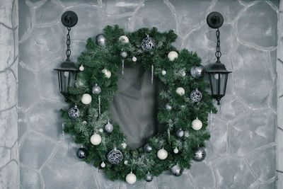 A christmas wreath with christmas decorations hangs on the wall near the lanterns