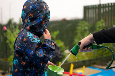 Cropped hand of person spraying water from hose in container held by child