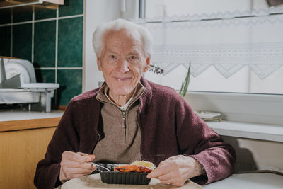 Portrait of smiling senior man eating food at home