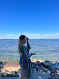 Side view of young woman looking at sea against clear blue sky