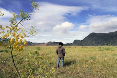 Rear view of woman standing on grassy field against sky