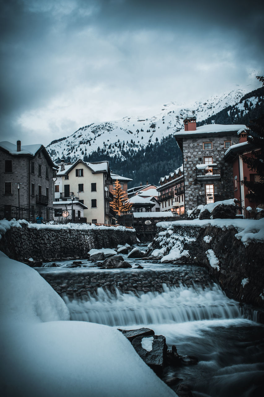 SNOW COVERED HOUSES BY BUILDINGS AGAINST SKY IN CITY