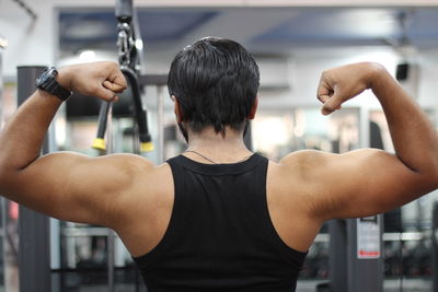 Rear view of man flexing muscles at gym