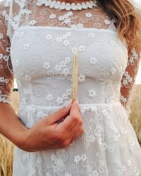 Midsection of woman wearing white dress holding wheat crop