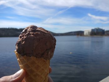 Close-up of hand holding ice cream over lake