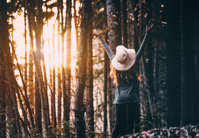 Rear view of woman playing with leaves while standing at forest