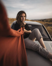 Portrait of woman sitting on top of a car against sky