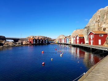 Buildings by river against clear blue sky