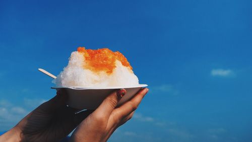 Close-up of hand holding flavored ice against blue sky