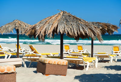 Lounge chairs on sand at beach against clear blue sky