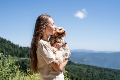 Young woman holding small dog puppy yorkshire terrier hiking at the mountains