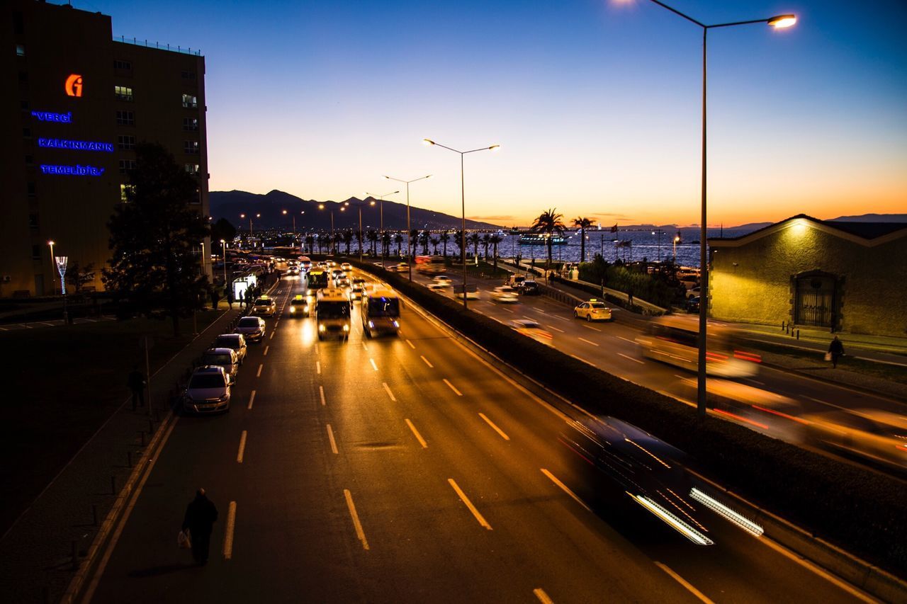 transportation, illuminated, city, road, car, building exterior, street light, traffic, street, mode of transport, road marking, land vehicle, architecture, built structure, city life, on the move, night, sunset, sky, city street