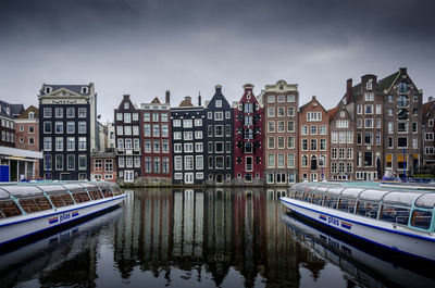 Buildings by canal against sky in city