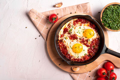 Flat lay image of shakshouka in a pan on a light coloured background close up