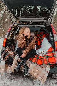 Blonde woman wrapped in blanket in trunk car. travel in winter. car decorated with festive christmas 