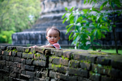 Portrait of baby boy standing by retaining wall against old ruin