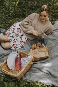 Smiling woman lying on blanket and reading book at summer day