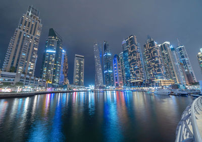 Illuminated city by river against sky at night