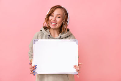 Portrait of smiling woman standing against pink background