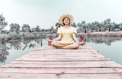 Woman practicing yoga and meditating in lotus position on wooden bridge.