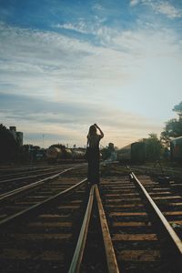 Rear view of woman standing on railroad tracks against sky