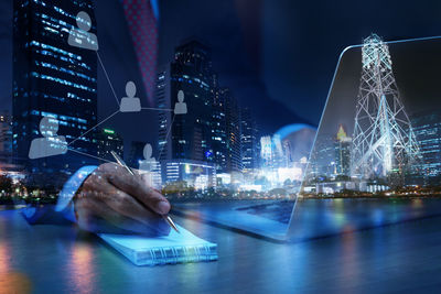 Digital composite image of businessman writing in book and illuminated cityscape