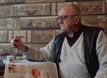 Senior man reading newspaper while stirring coffee in cafe