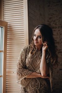 Smiling young woman looking through window while standing at home