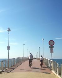 Rear view of father and son riding bicycles on pier against sky