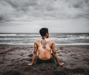 Rear view of shirtless man on beach against sky