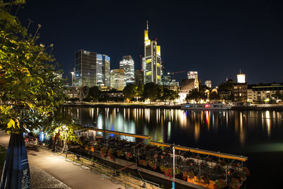 Illuminated buildings by river against sky in city at night