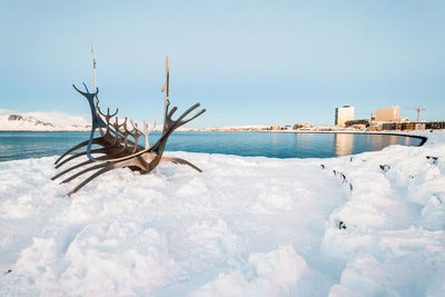 Snow covered land by sea against sky