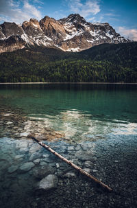 Scenic view of wooden log and lake by snowcapped mountains - eibsee germany