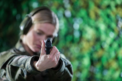 A lady soldier at a shooting range aims a pistol at a target with headphones on her ears.