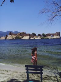 Woman sitting on bench at beach against clear sky