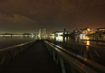 Pier over lake by illuminated city at night