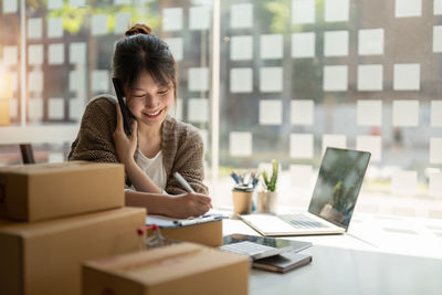 Businesswoman talking on phone while writing in diary at office