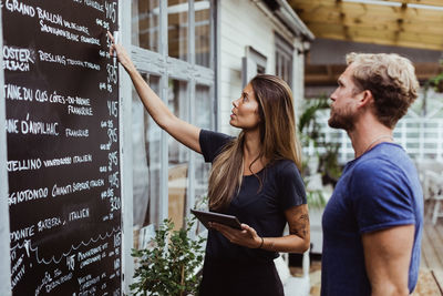 Businesswoman with digital tablet pointing at wall while standing with coworker in restaurant