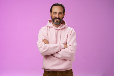 Smiling man with arms crossed against purple background