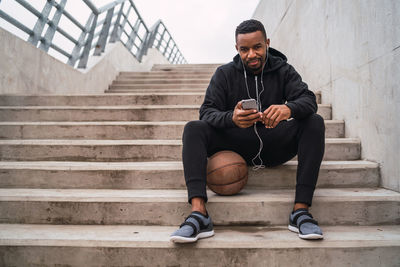 Portrait of man listening music while sitting on steps with basketball