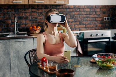 Athletic young woman in a virtual reality headset at home in her kitchen orders food, smart home